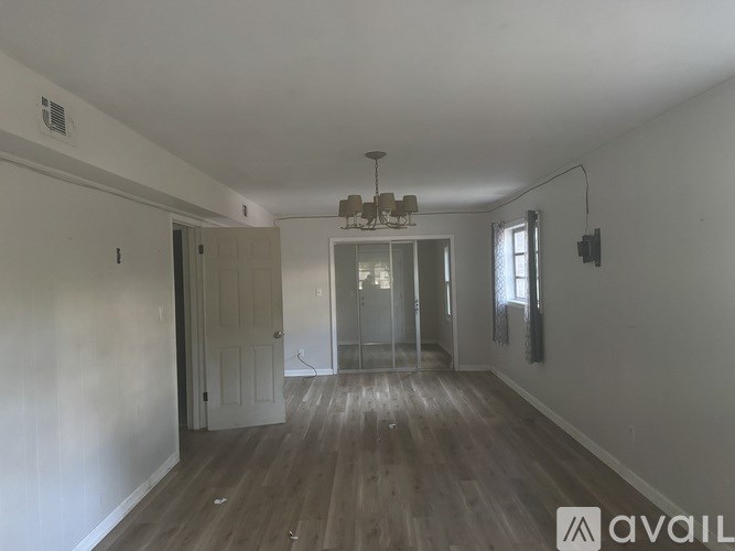 A spacious room with wooden floors and a chandelier hanging from the ceiling.