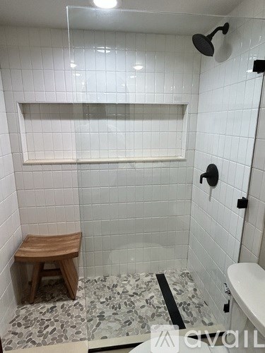 A white tiled bathroom with a wooden stool and a glass shower door.