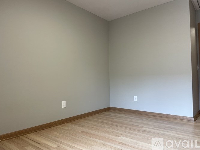 A room with wooden flooring and two switches on the wall.