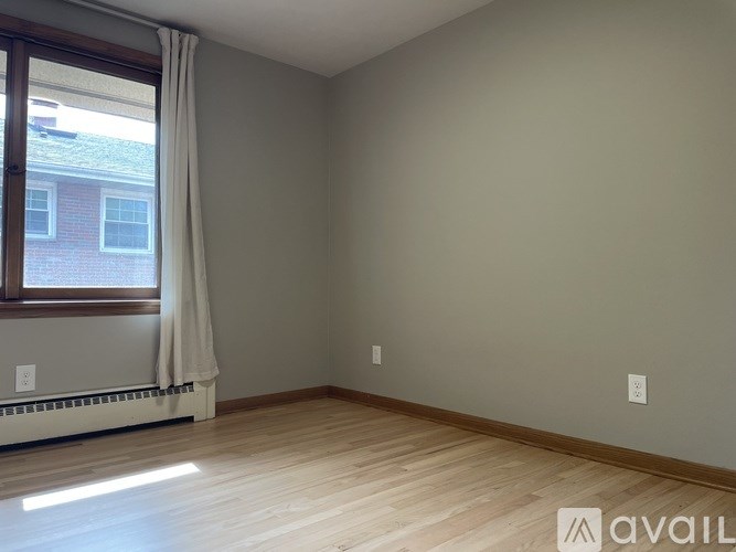 A room with wooden flooring and a window with white curtains.