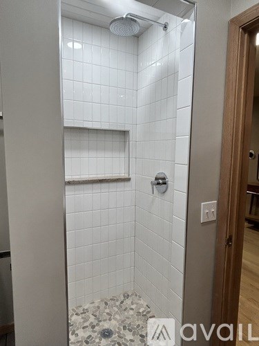 A white tiled shower with a glass door and a brown door frame.