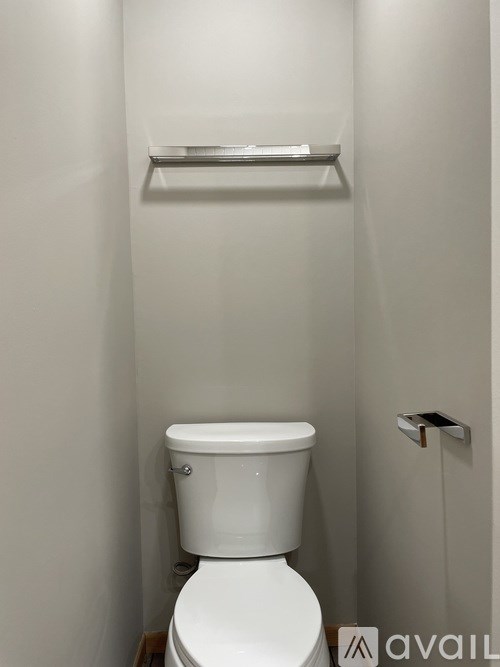 A white toilet in a small bathroom with a shelf above it.