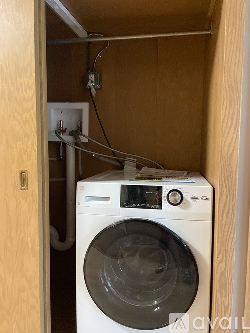 A white washing machine in a small room with wooden walls.
