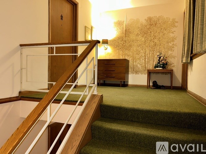 A staircase with a green carpet and a wooden handrail.