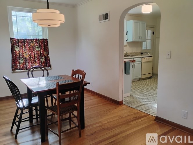 A dining room with a table and chairs and a kitchen in the background.