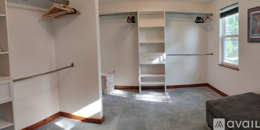 A room with a grey ottoman and a white closet with shelves.