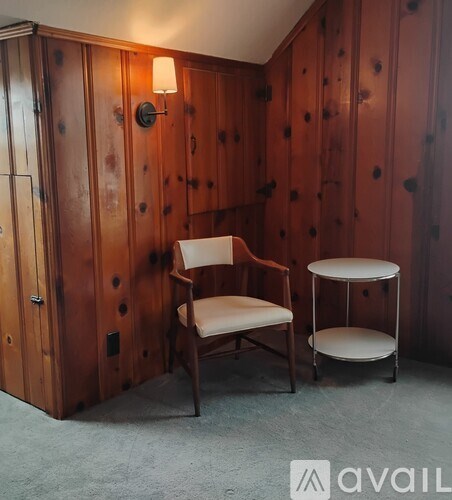 A wooden chair with a white cushion is placed in front of a wooden wall with a light on it.