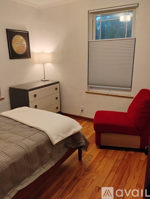 A bedroom with a bed, a red chair, and a dresser with a lamp on it.