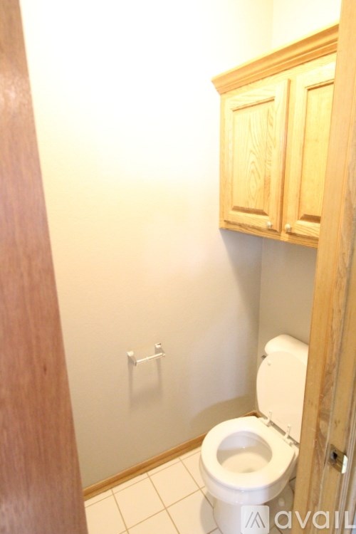 A white toilet in a small bathroom with wooden cabinets.