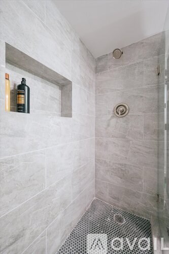 A bottle of soap is on a shelf in a tiled shower.