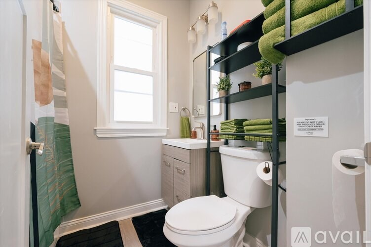 A bathroom with a toilet, sink, and shelves with green towels.