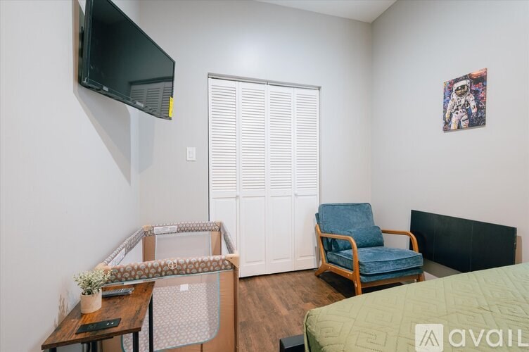 A room with a bed, chair, and television mounted on the wall.