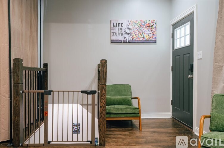 A baby crib sits next to a green chair in a room with a poster on the wall that says "Life is Beautiful".