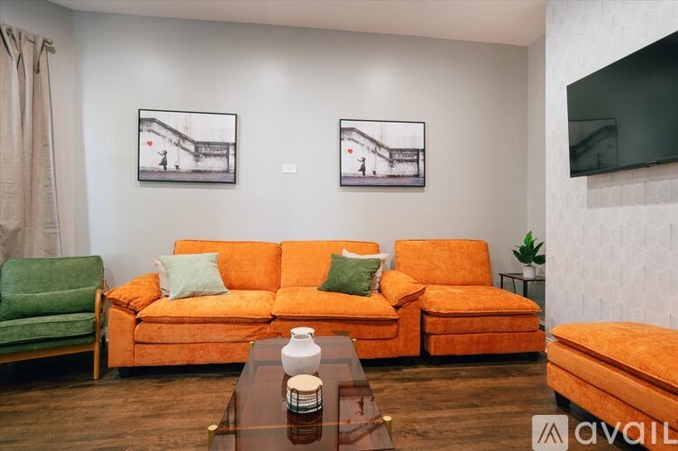 A living room with a green chair, orange couch, and two pictures on the wall.