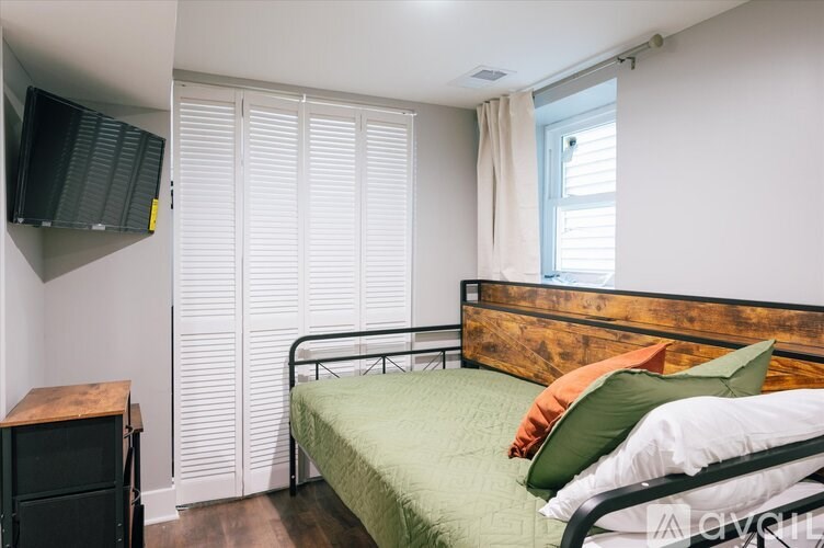 A bedroom with a bed, a nightstand, and a window with blinds.