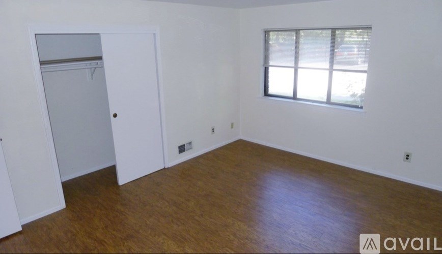 A room with a wooden floor and a window with blinds.