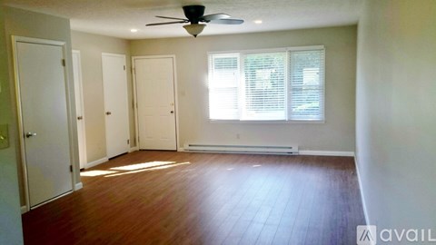 A room with a fan, wooden floors, and three doors.