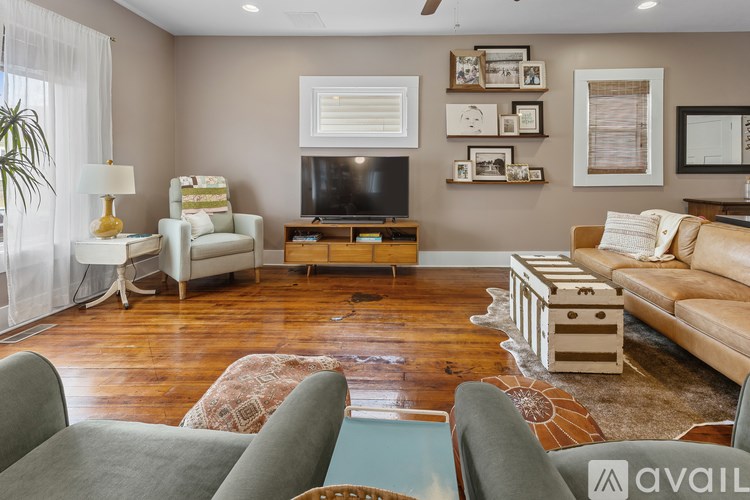 A living room with a grey sofa, a green armchair, a white chair, a wooden coffee table, and a television on the wall.