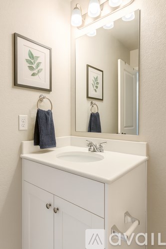 A bathroom with a white sink and a mirror with lights around it.