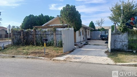 A house with a white fence and a gate is surrounded by trees and bushes.