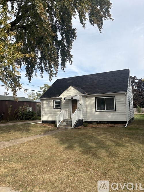 A small house with a porch and a tree in front.