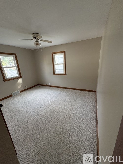 A room with a carpeted floor, a ceiling fan, and two windows.