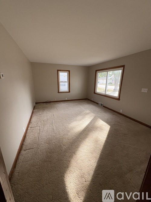 A room with a carpeted floor and two windows.