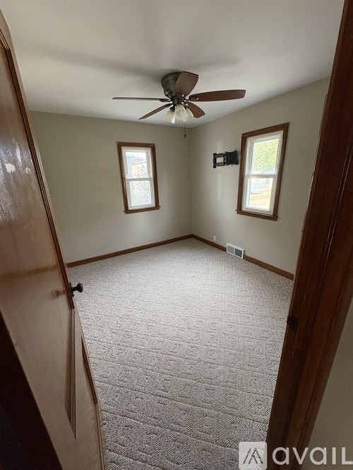 A room with a ceiling fan and two windows.