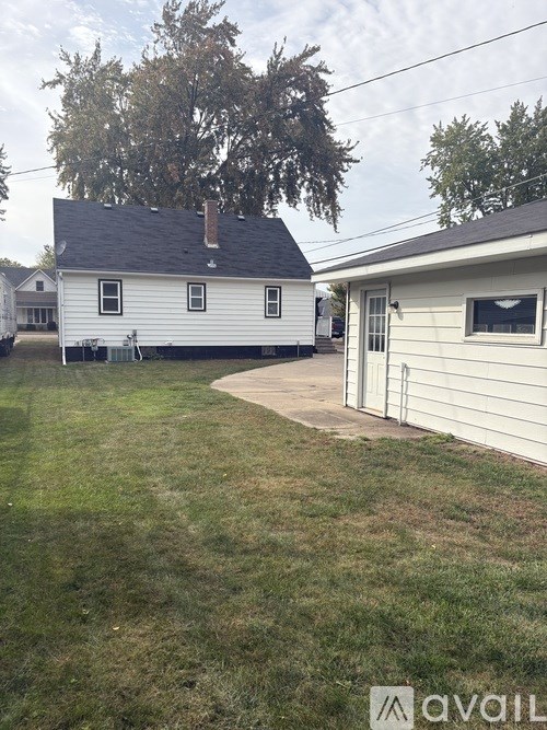 A white house with a black roof and a tree in the backyard.