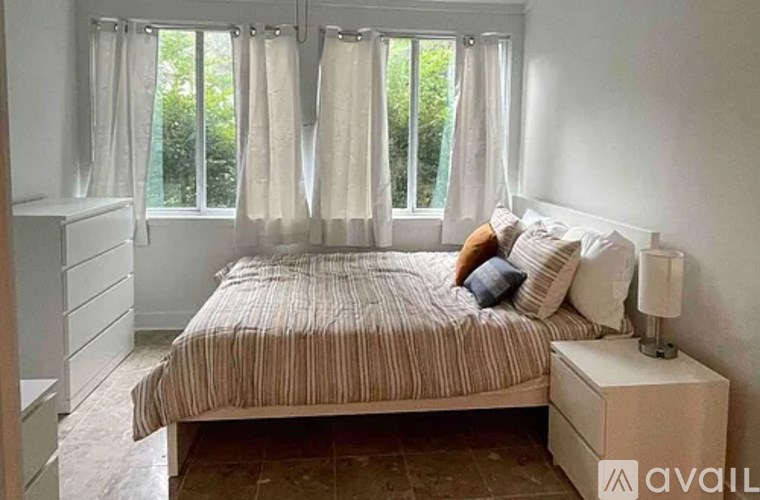 A bedroom with a bed, nightstand, and window with curtains.