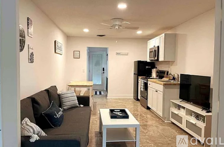 A living room with a couch, a coffee table, and a kitchen area in the background.