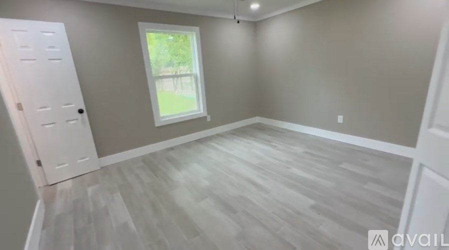 A room with light grey walls and a window with a view of a green area outside.