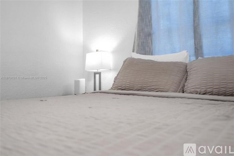 A bedroom with a bed, pillows, a lamp, and a window with curtains.