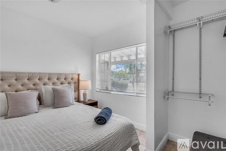 A bedroom with a bed, pillows, a lamp, and a window with blinds.