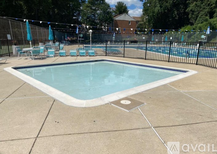 A pool surrounded by a black fence with blue umbrellas and chairs.