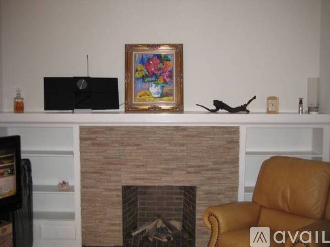 A black laptop sits on a white shelf above a fireplace with a colorful painting and a wooden airplane model.