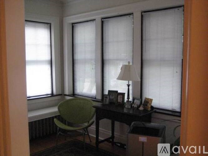 A room with a green chair, a table with a lamp and some pictures on it.