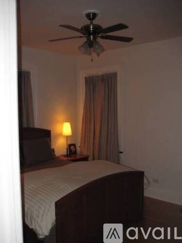 A bedroom with a bed, a ceiling fan, and a lamp.