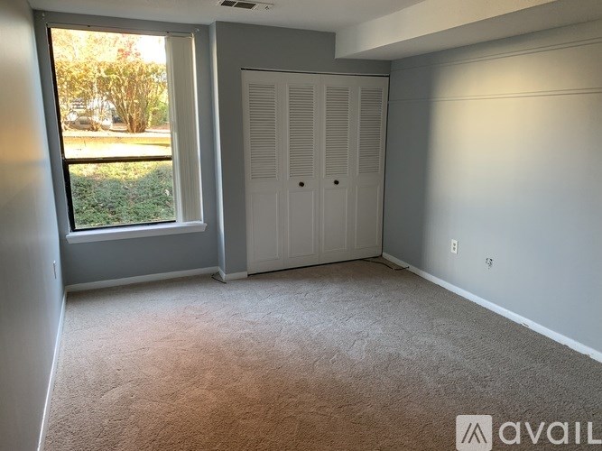 A room with a carpeted floor, a window, and a white door.