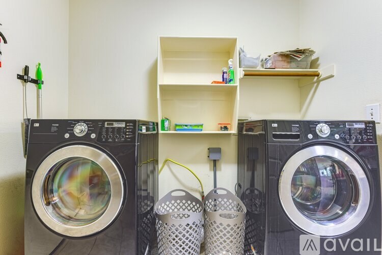 A laundry room with two front-loading washing machines and a shelf above them.
