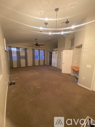 A spacious room with a ceiling fan and a refrigerator in the corner.