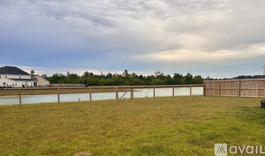 A grassy field with a fence and a house in the background.