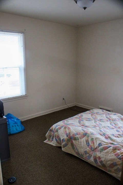 A bedroom with a bed, a window, and a blue bag on the floor.