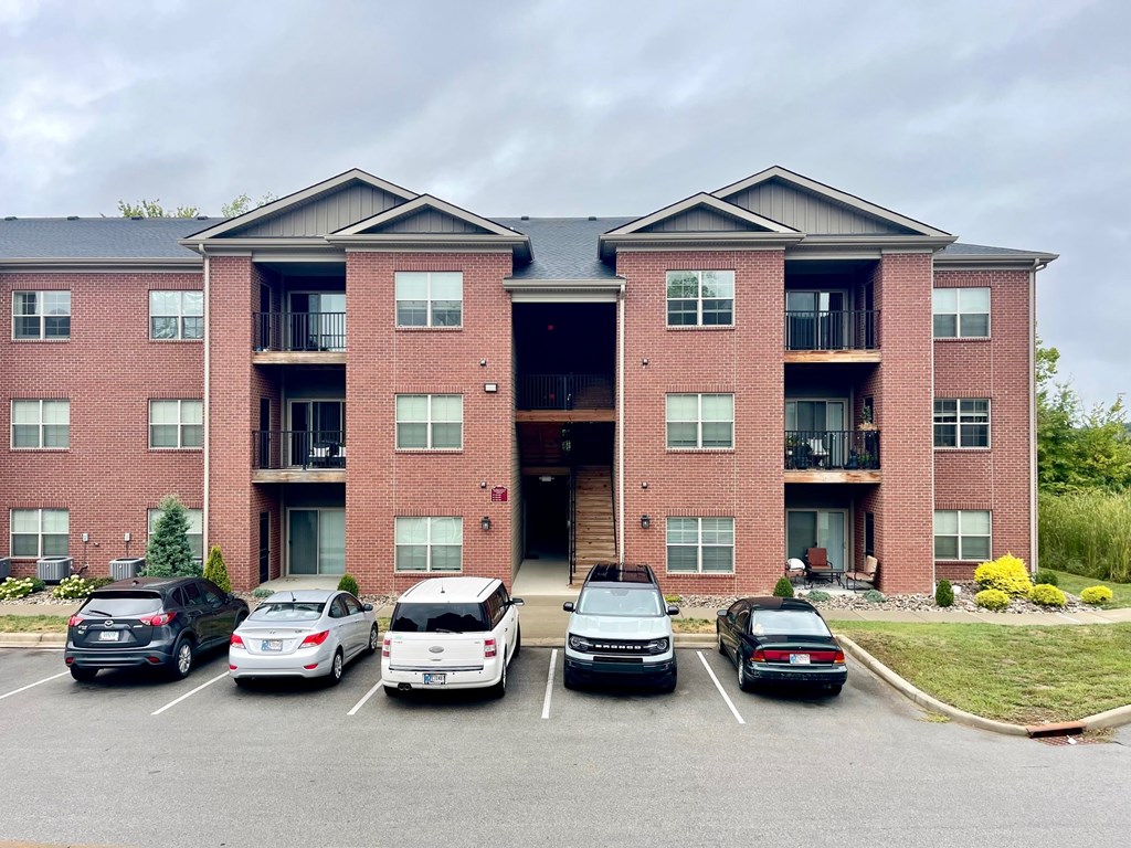 A parking lot in front of a red brick apartment building with cars parked.