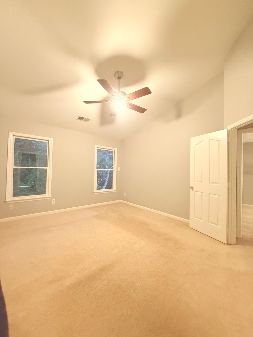 A room with a ceiling fan and two windows.