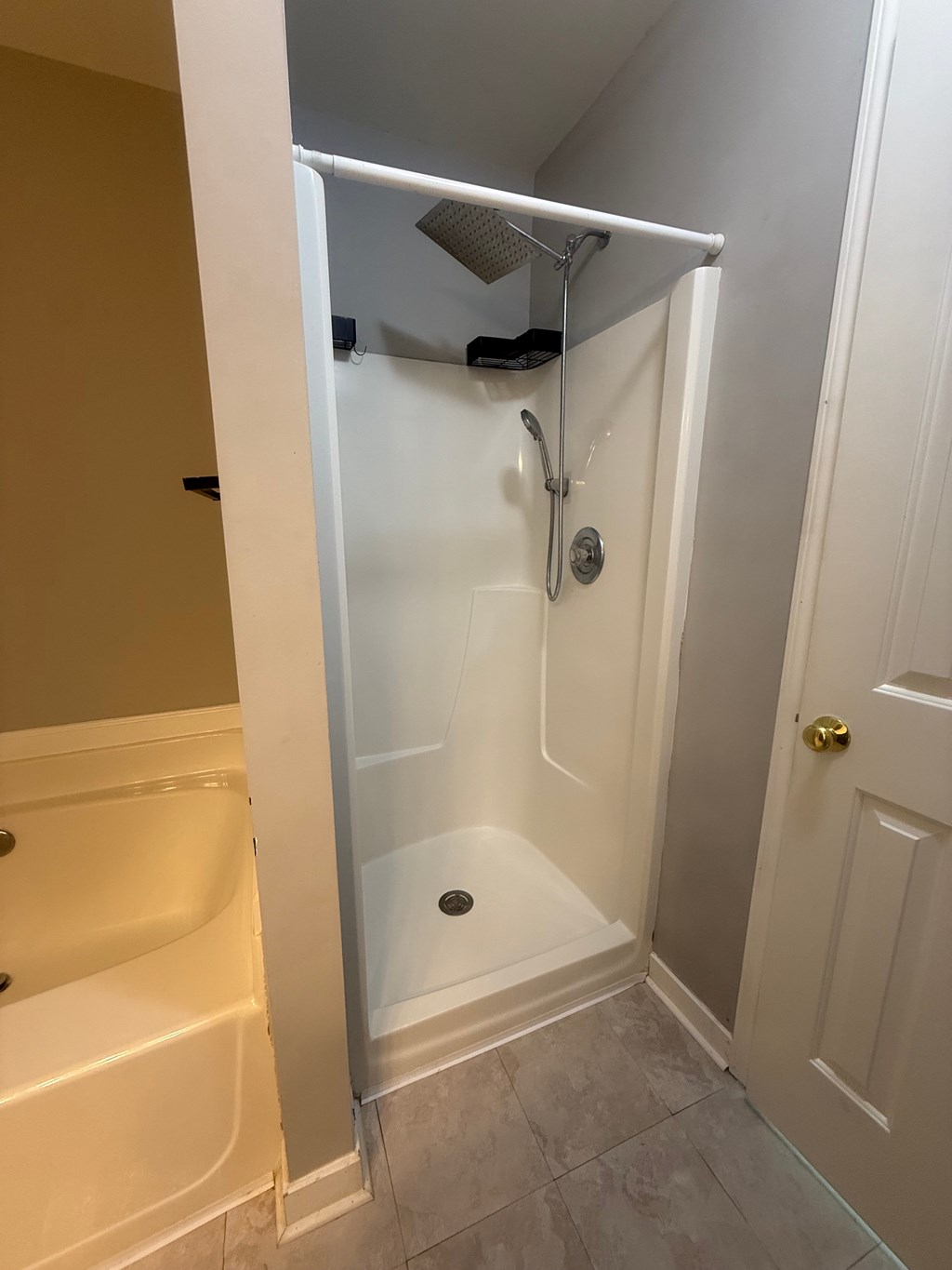 A white shower stall with a door open to a bathroom.