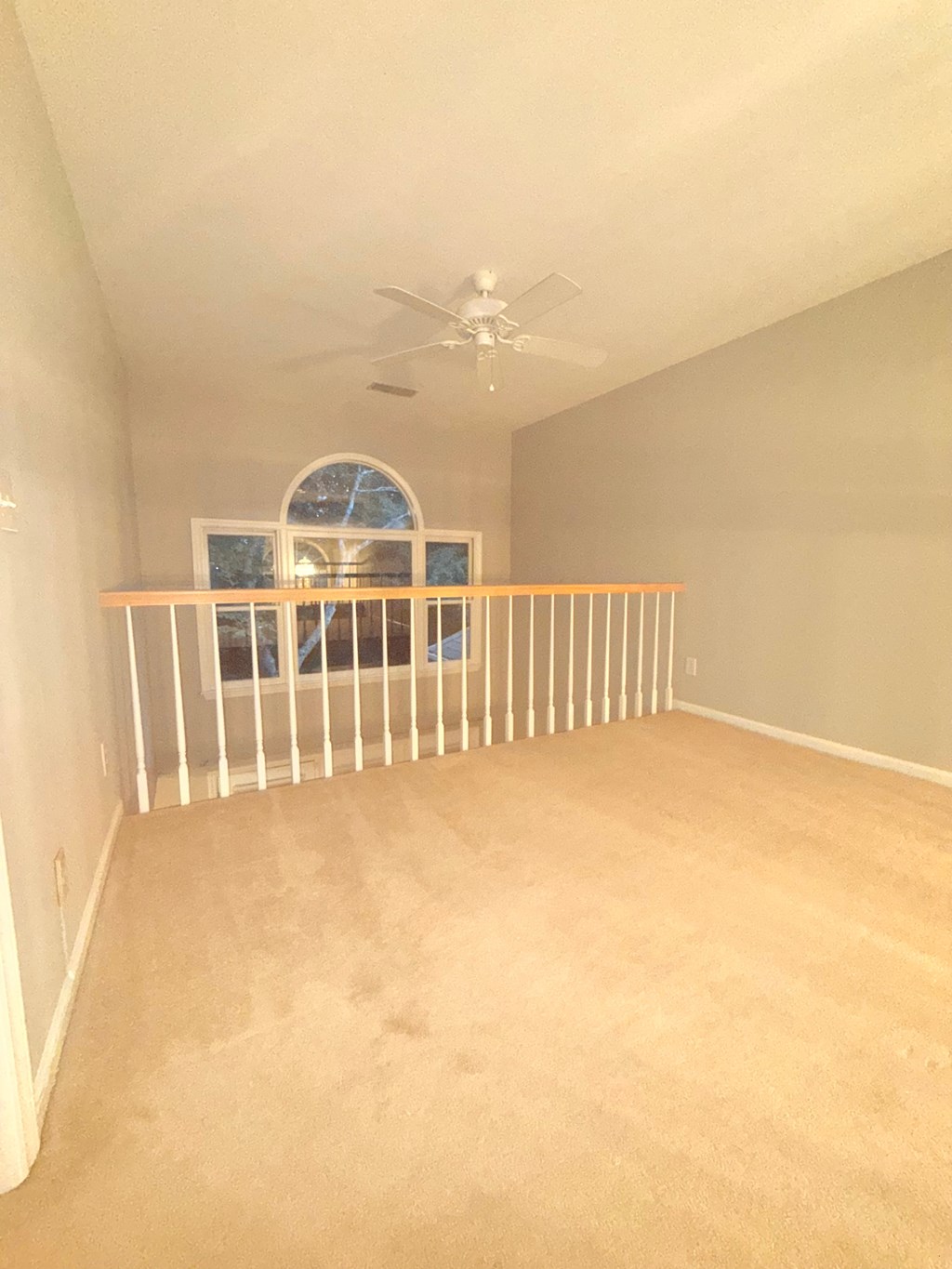A room with a ceiling fan and a window with a view of trees.