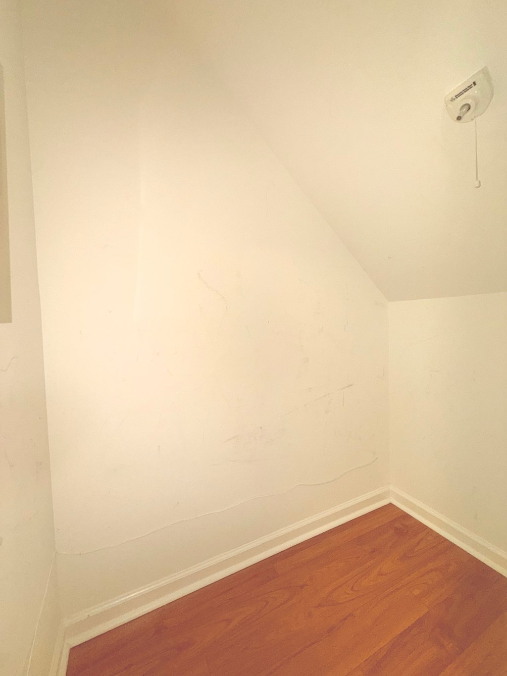A room with a wooden floor and a smoke detector on the ceiling.