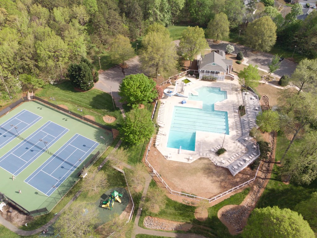 An aerial view of a tennis court and a swimming pool surrounded by trees.