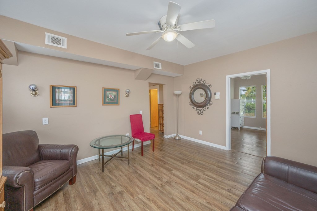 A living room with a brown leather couch, a glass table, and a ceiling fan.